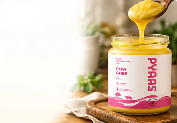 Golden ghee poured from a wooden spoon into a jar of PYAAS cow ghee